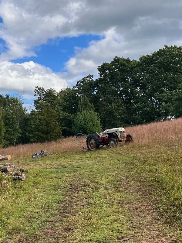 Tractor working cleared 10-acre agricultural field at AI Sustainable Foods closed-loop farm campus with Pocono Mountain treeline and container infrastructure visible Saylorsburg Pennsylvania